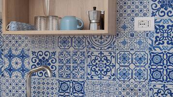 A kitchen with a stainless steel sink, a wooden cabinet above it, and blue patterned tiles on the wall.