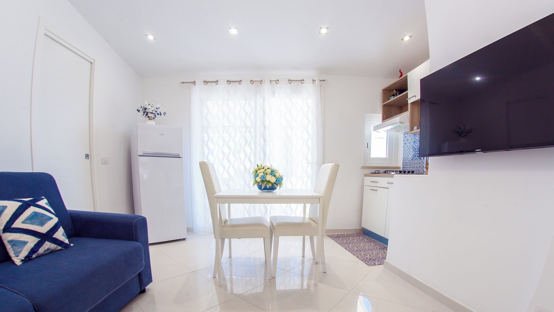 A compact living space with a kitchenette, a dining area with a table and chairs, and a sofa.