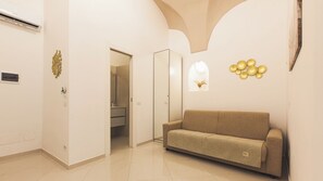 A modern interior with a beige sofa, a glass door leading to a bathroom, and decorative wall art. - LA PERLA AZZURRA (Gaeta)