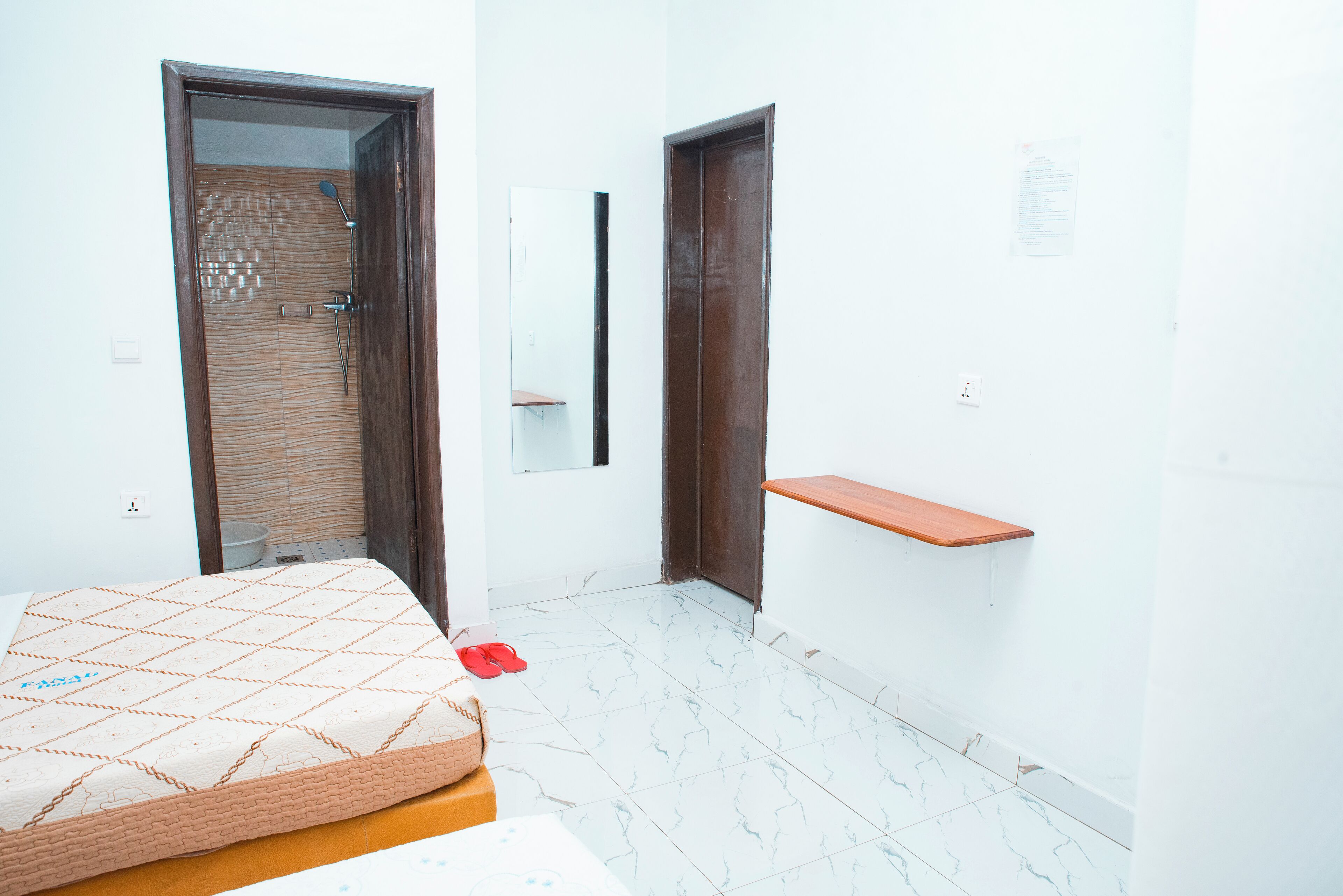 A bedroom with a bed, a wooden door, a mirror, and a small wooden shelf.