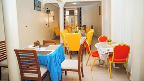 A dining area with yellow and red chairs, a blue tablecloth, and a white table. - Fanad Hotel (Gisenyi)