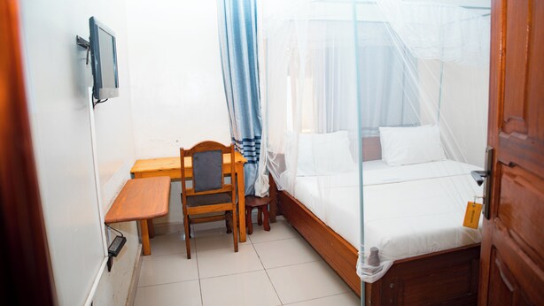 Un dormitorio con cama de madera, un escritorio pequeño, una silla y un televisor instalado en la pared.