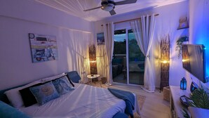 A bedroom with a bed, a ceiling fan, a TV, and a sliding glass door leading to an outdoor area. - Andros Apt 2 Bed Free Wi-fi Safe Complex Pool (Paralimni)