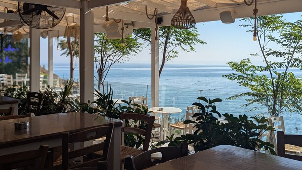 An outdoor dining area with tables and chairs, overlooking a body of water. - Andros Apt 2 Bed Free Wi-fi Safe Complex Pool (Paralimni)