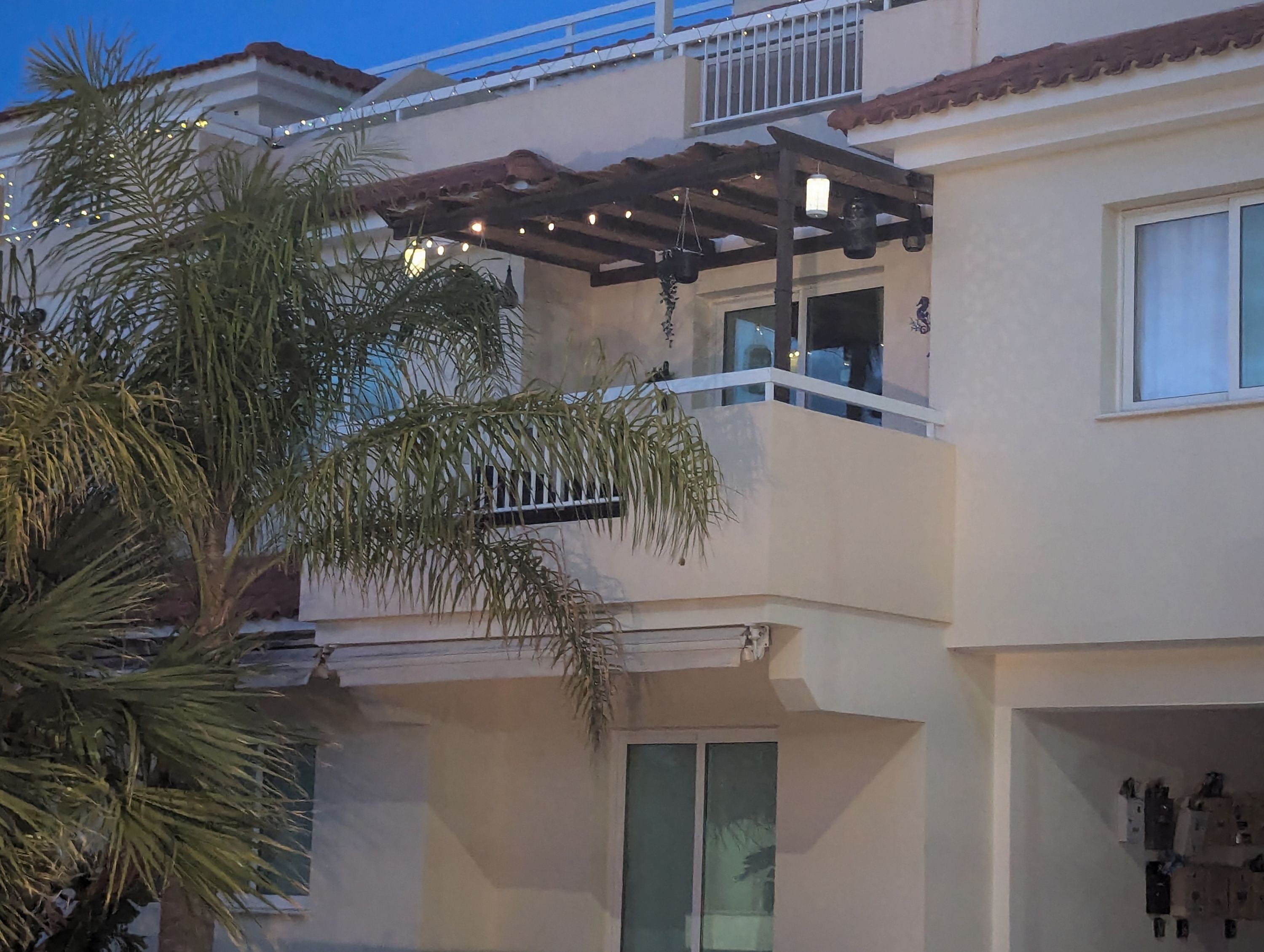 A multi-story building with a balcony, string lights, and a palm tree.