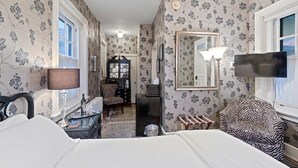 Ein Hotelzimmer mit einem Bett, einem Schreibtisch mit Lampe, einem Sessel, einem Fernseher und einem Spiegel.