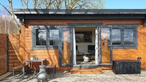 Une cabane en bois dotée d’un patio comprenant une table et des chaises, ainsi qu’un petit chauffage d’extérieur.