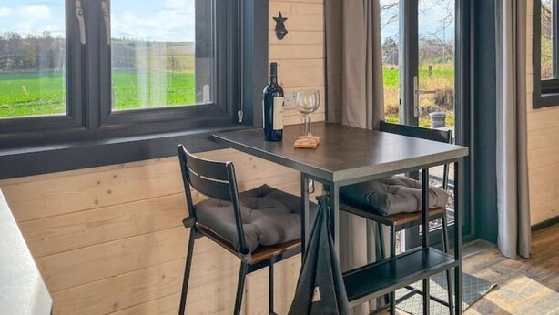 A dining area with a table and chairs, a bottle of wine, and a glass. - Barn Owl Cabin at Redroofs - Pet Friendly! (Forfar)