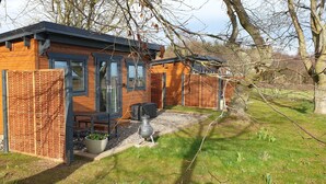 A small wooden cabin with a black roof, a fenced garden, and a metal pot on the ground. - Barn Owl Cabin at Redroofs - Pet Friendly! (Forfar)