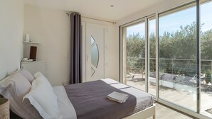 A bedroom with a bed, a bedside table, a mirror, a window, and a balcony. - Luxury Villa – Panoramic Views of Mountains, Wi-Fi, and Air Conditioning (Volx)