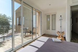 A modern bedroom with a large sliding glass door leading to a balcony, a bed with a white blanket, and a wooden drying rack.
