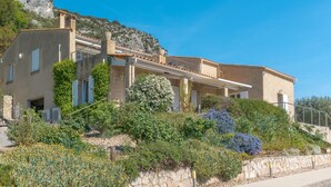 A Mediterranean-style villa with a stone facade, a balcony, and lush vegetation. - Luxury Villa – Panoramic Views of Mountains, Wi-Fi, and Air Conditioning (Volx)