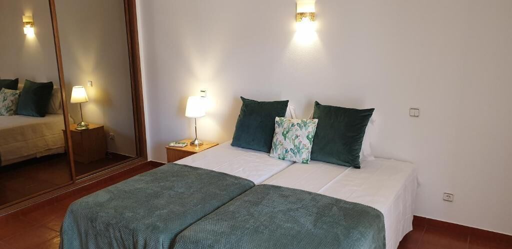 A double bed with green bedding, a bedside table with a lamp, and a mirror on the wall.