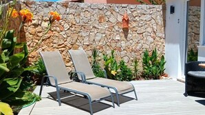 A sunlit outdoor area with two lounge chairs, a stone wall, and potted plants. - Dona Ana Guesthouse (Lagos)