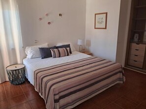 A bedroom with a bed, bedside table, lamp, and a wall with a framed picture. - Dona Ana Guesthouse (Lagos)