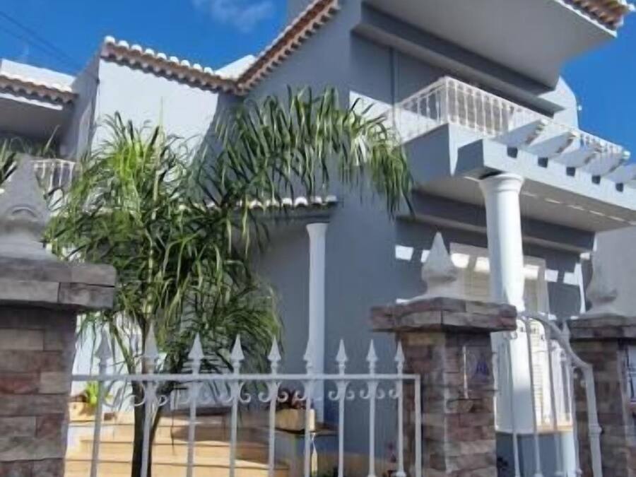 A modern house with a white exterior, a tiled roof, and a white fence with decorative elements.