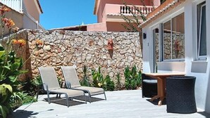 A patio with two lounge chairs, a table, and a stone wall. - Dona Ana Guesthouse (Lagos)