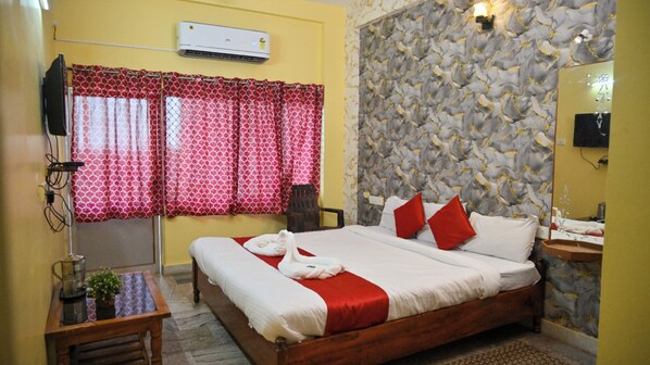 A hotel room with a bed, a bedside table with a coffee maker, a mirror, and a window with patterned curtains.