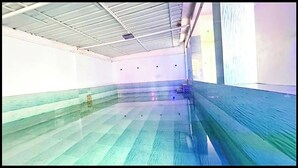 Una piscina interior con suelo de baldosas y techo con vigas a la vista.