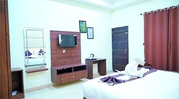 Habitación de hotel con cama, televisor montado en la pared, armario, espejo y cortina.