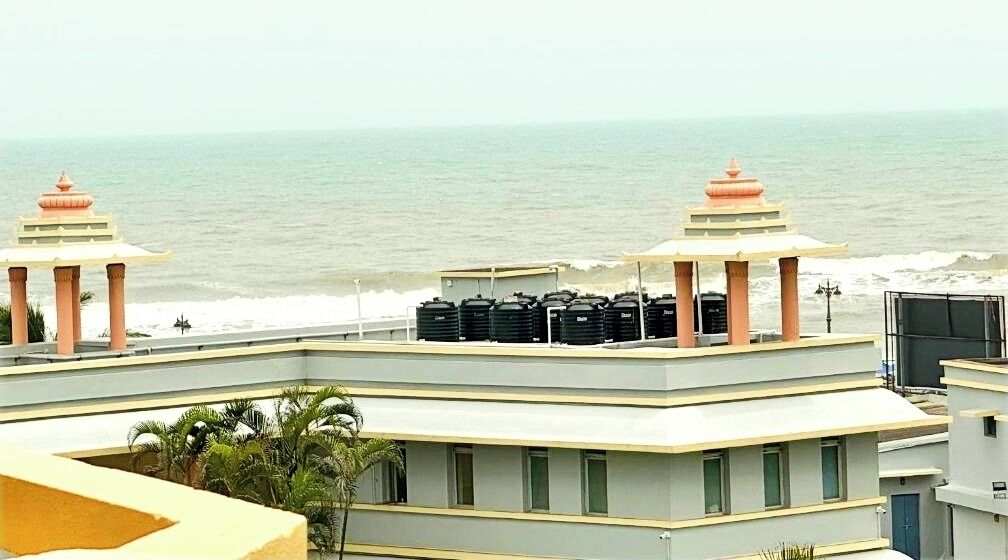 Un hotel con terraza en la azotea que da al mar, con dos pabellones de estilo tradicional y una hilera de depósitos de agua.
