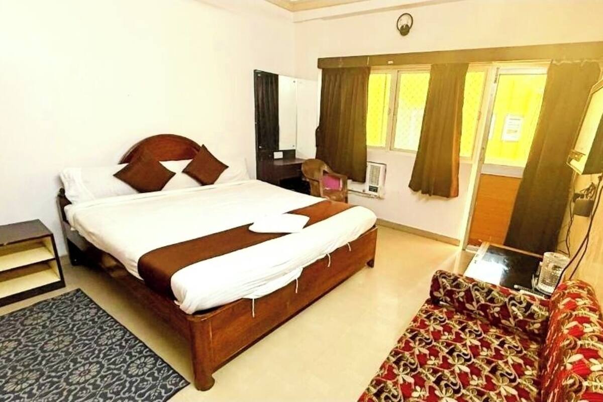 Een hotelkamer met een bed, een slaapbank, een bureau en een raam met gordijnen.