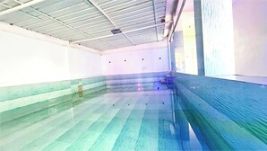 Una piscina interior con suelo de baldosas y techo con vigas a la vista.