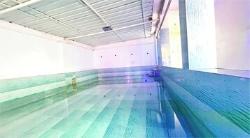 Una piscina interior con suelo de baldosas y techo con vigas a la vista.