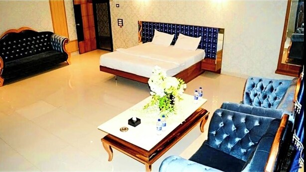 Una habitación de hotel con cama, sofá, sillón y una mesa de centro con flores.
