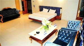 A hotel room with a bed, a sofa, a chair, and a coffee table with flowers.