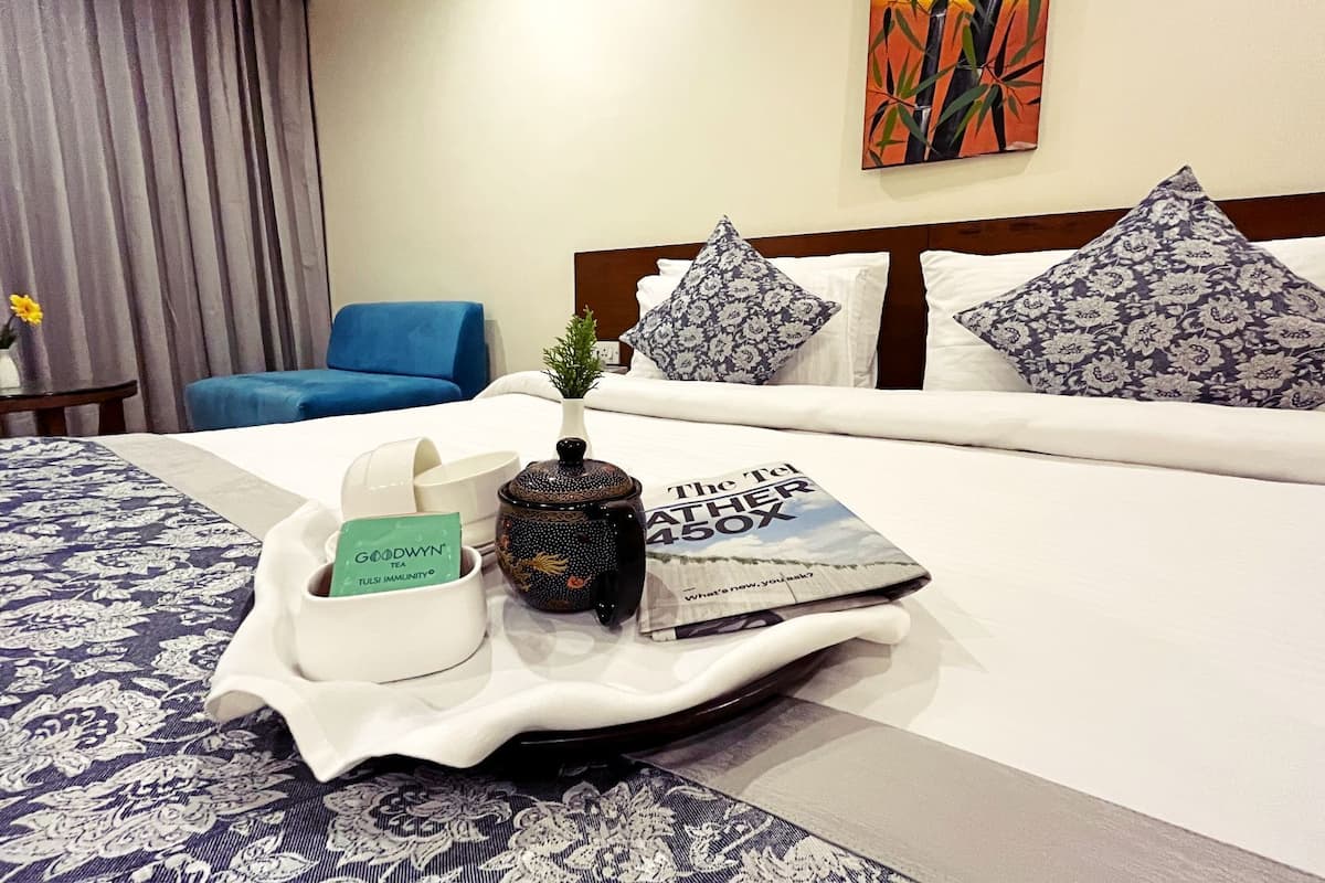 A neatly made hotel bed with a tray of amenities including a tea set, a book, and a small plant.