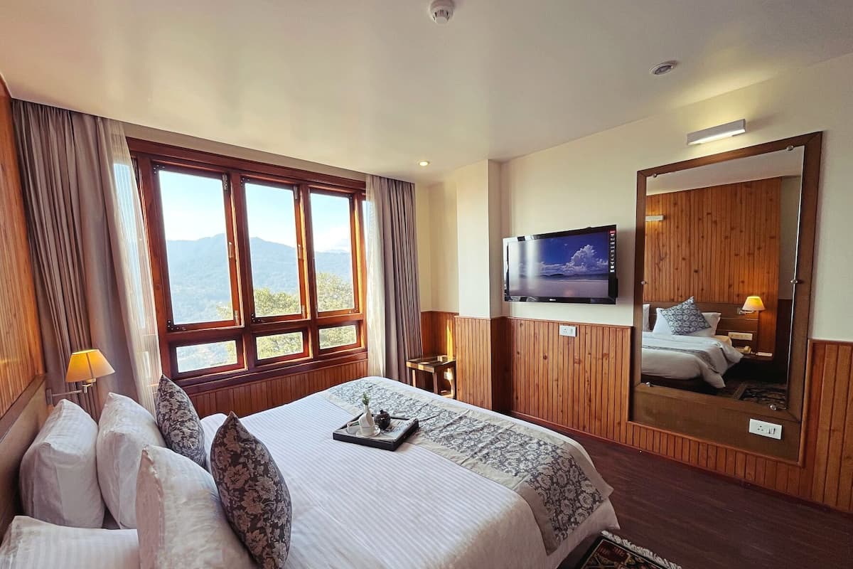A hotel room with a large bed, a TV, a mirror, and a window with a mountain view.