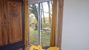 A room with a bed, a wooden wardrobe, and a view of a garden through a glass door. - Gîte 4 persons Mathys (Doissat)