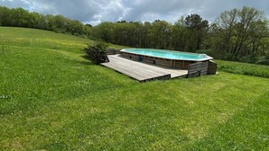 A swimming pool with a wooden deck, surrounded by a grassy field and trees. - Gîte 4 persons Mathys (Doissat)