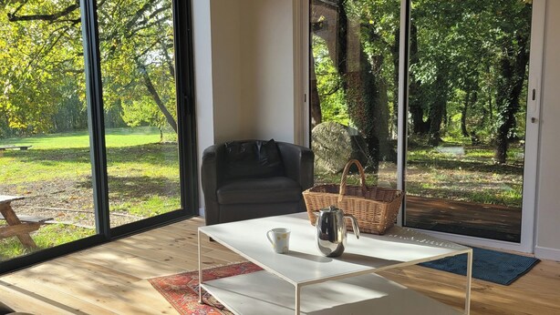 A modern room with large windows, a black leather sofa, a white coffee table, and a wicker basket. - Gîte 4 persons Mathys (Doissat)