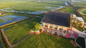 Una casa moderna con tetto spiovente, circondata da rigogliosi campi verdi e canali d'acqua.