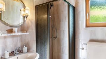 Een badkamer met douche, wastafel, spiegel en toilet.