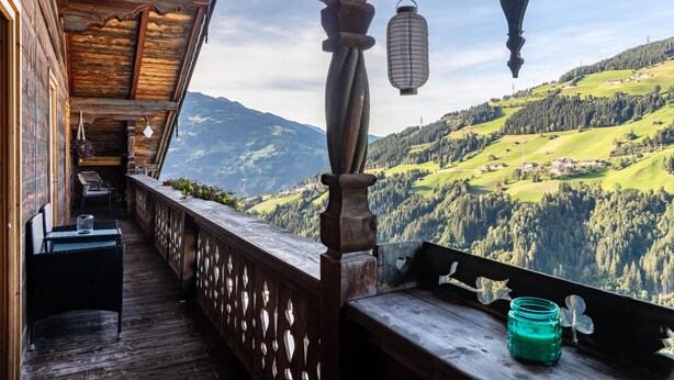 A wooden balcony with a view of a green valley and mountains.