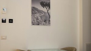 Una habitación con una fotografía en blanco y negro enmarcada de un paisaje, una pequeña mesa, dos sillas y un interruptor de luz en la pared.