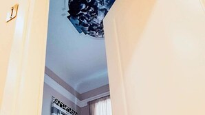 A narrow hallway leading to a bedroom with a bed, a nightstand, and a wall-mounted artwork.