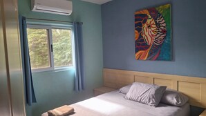 Un dormitorio con cama, almohadas, un cuadro, aire acondicionado y una ventana con cortinas.