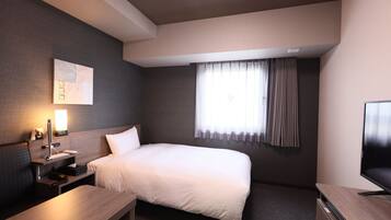 Una habitación de hotel moderna con una cama grande, un escritorio, un televisor de pantalla plana y un ventanal con cortinas.