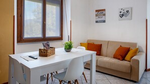 A room with a white table, a beige sofa with orange cushions, a window with blinds, and wall decorations including a sign and a heart-themed picture. - Apartment 'La Terrazza' with Mountain View, Wi-Fi and Air Conditioning (Nesina)