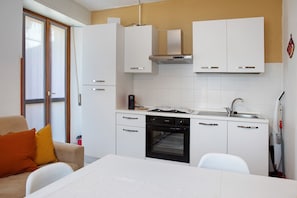 Une cuisine de taille réduite avec des meubles blancs, un four encastré et une fenêtre.