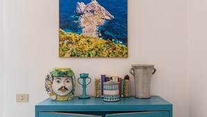 A teal cabinet with a painting of a rocky island, a ceramic jug, a decorative vase, and several books.