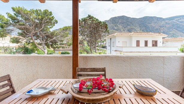 A wooden table with a bowl of flowers, a fish-shaped plate, and a bowl on a balcony overlooking a mountainous landscape.
