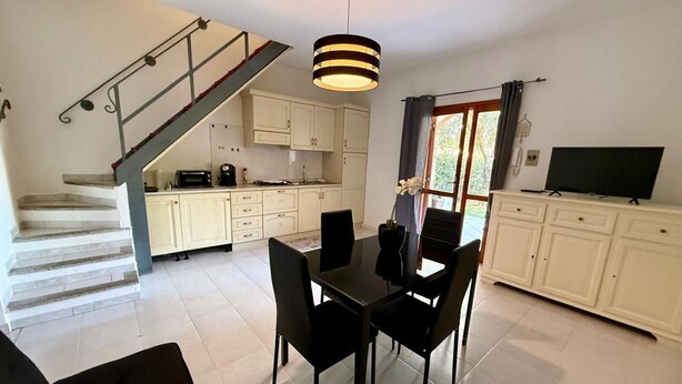 Een eetruimte met een tafel en stoelen, een trap en een keuken met kasten en apparatuur.