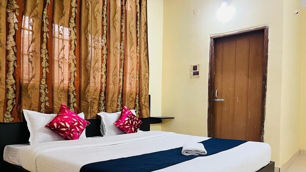 A neatly made bed with white and blue bedding, two pillows, and a folded towel. A wooden door is visible to the right. - Hotel Cosy Home (Guwahati)