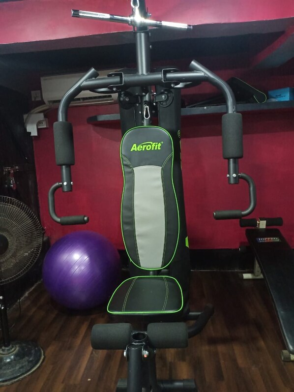 A gym with an Aerofit exercise machine, a purple exercise ball, and a fan.