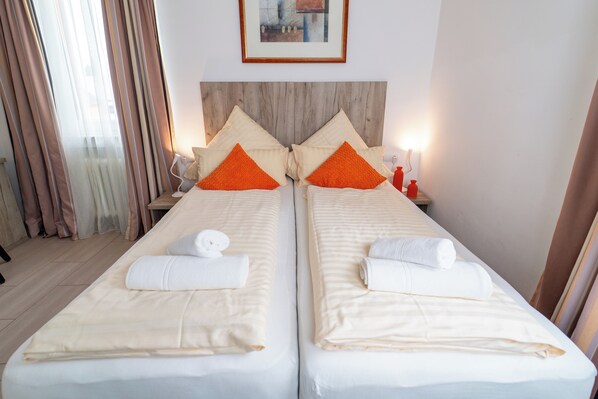 A double bed with white linens and orange pillows, a bedside table with a lamp, and a framed picture on the wall. - Hotel Lichtblick (Salach)